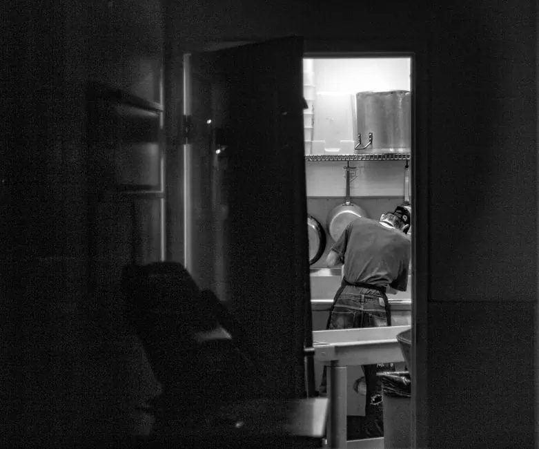 Black and white photo of a dishwasher working in an industrial kitchen setting.